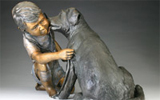 Statue of a little boy kneeling down as a dog licks his cheek.