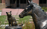 Statue of a young filly looking at a cat on a pedestal.