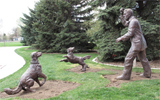 Statue of Mr. Stuart playing fetching with two golden retriever dogs.